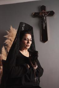 A woman in a mantilla praying with a rosary in her hands
