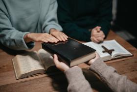 Group of Christians sit together and pray around a wooden table